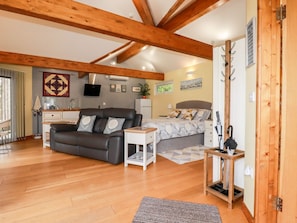 A cozy room with a sofa, a bed, a small table, and a wooden ceiling structure. - Brambleside Lodge (Truro)