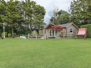 A wooden cabin with a deck, surrounded by a well-maintained lawn and trees. - Brambleside Lodge (Truro)