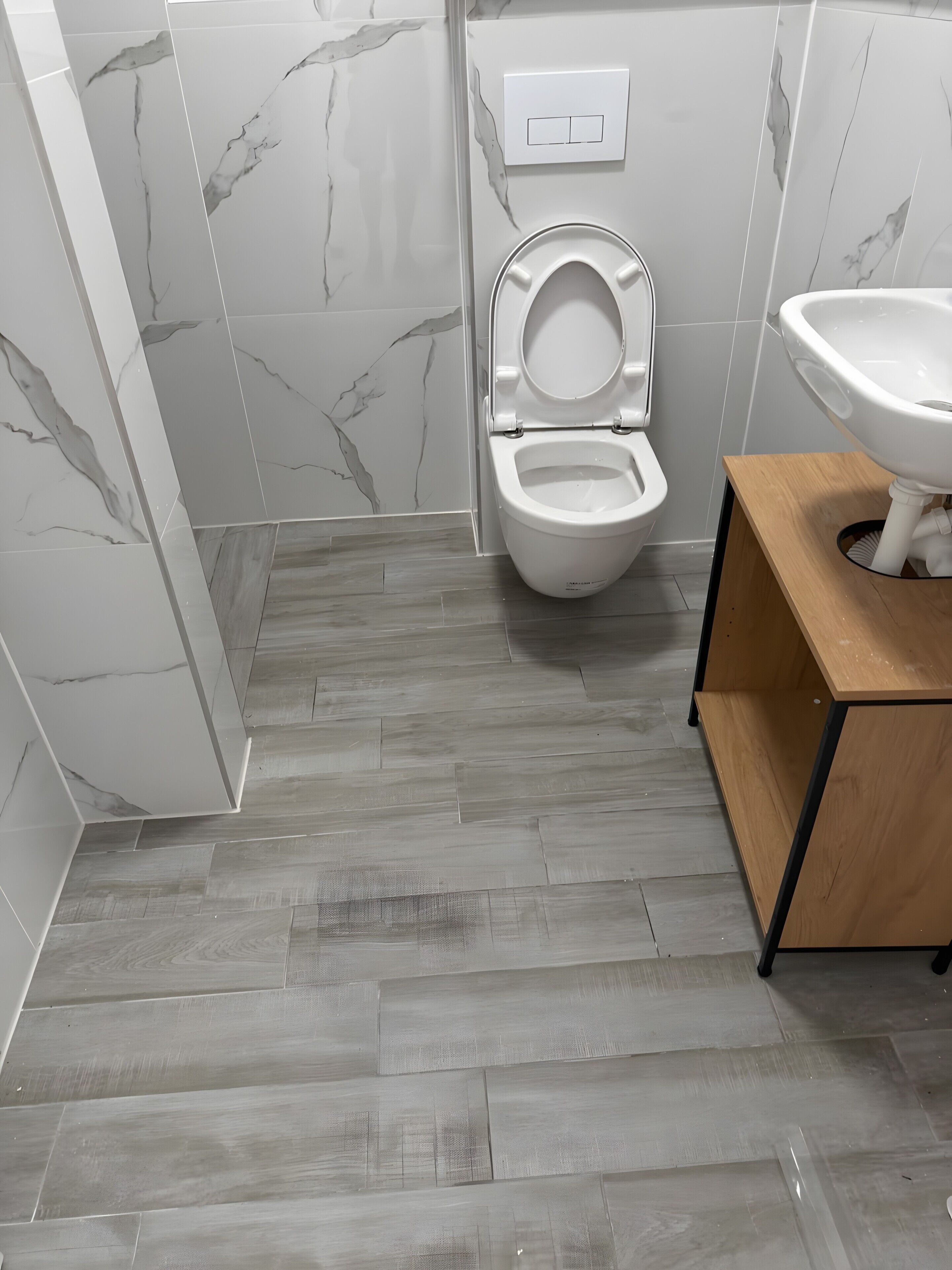 A bathroom with a toilet, a sink, and a wooden vanity.