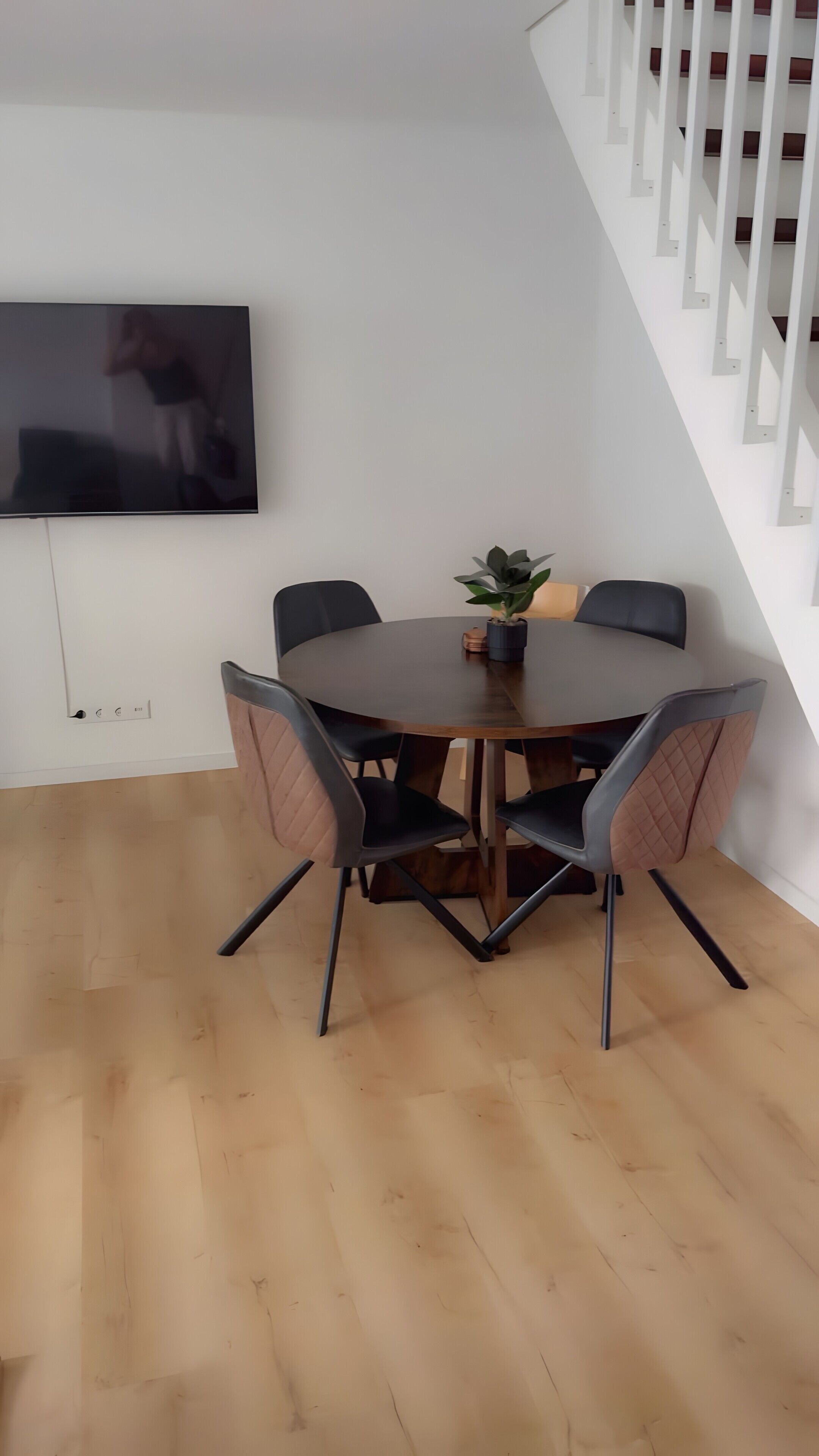 A round dining table with six chairs, a potted plant, and a flat-screen TV mounted on the wall.