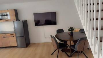 A modern kitchen with a built-in refrigerator, a dining area with a round table and chairs, and a flat-screen TV mounted on the wall.