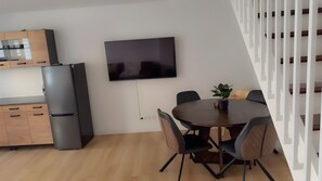 A modern kitchen with a built-in refrigerator, a dining area with a round table and chairs, and a flat-screen TV mounted on the wall.