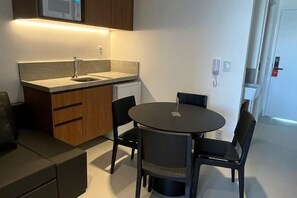 A compact kitchen with a built-in microwave, a sink, and a round dining table with four chairs. - Apartment Muro Alto (N. Sra. do Ó)