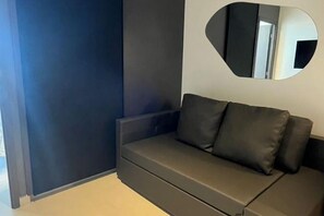 A modern room with a dark-colored sofa against a wall, a round mirror, and a partial view of a door. - Apartment Muro Alto (N. Sra. do Ó)