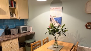 Eine Küche mit einem Holztisch, Stühlen, einer Mikrowelle, einem Mülleimer und einem Poster an der Wand.