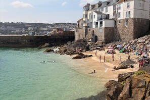 Zona costera con playa de arena, costa rocosa y edificios de paredes de piedra.