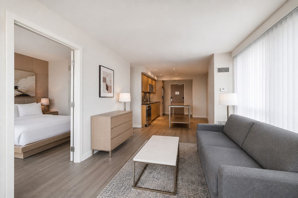 Ein modernes Hotelzimmer mit Bett, einer Couch, einem Esstisch und einer Küchenzeile.
