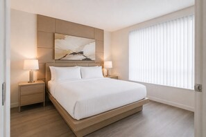 Ein modernes Schlafzimmer mit einem Bett, zwei Nachttischen und einem großen Fenster mit Jalousien.