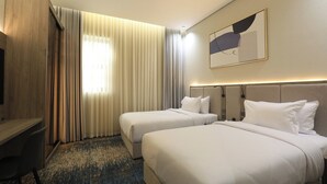 Ein Hotelzimmer mit zwei Betten, einem Schreibtisch und einem großen Fenster mit Vorhängen.