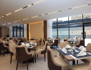 A spacious dining area with multiple tables and chairs, large windows, and a modern ceiling design. - Azara Hotel (Riyadh)