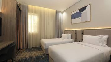 A hotel room with two beds, a desk, and a large window with curtains.