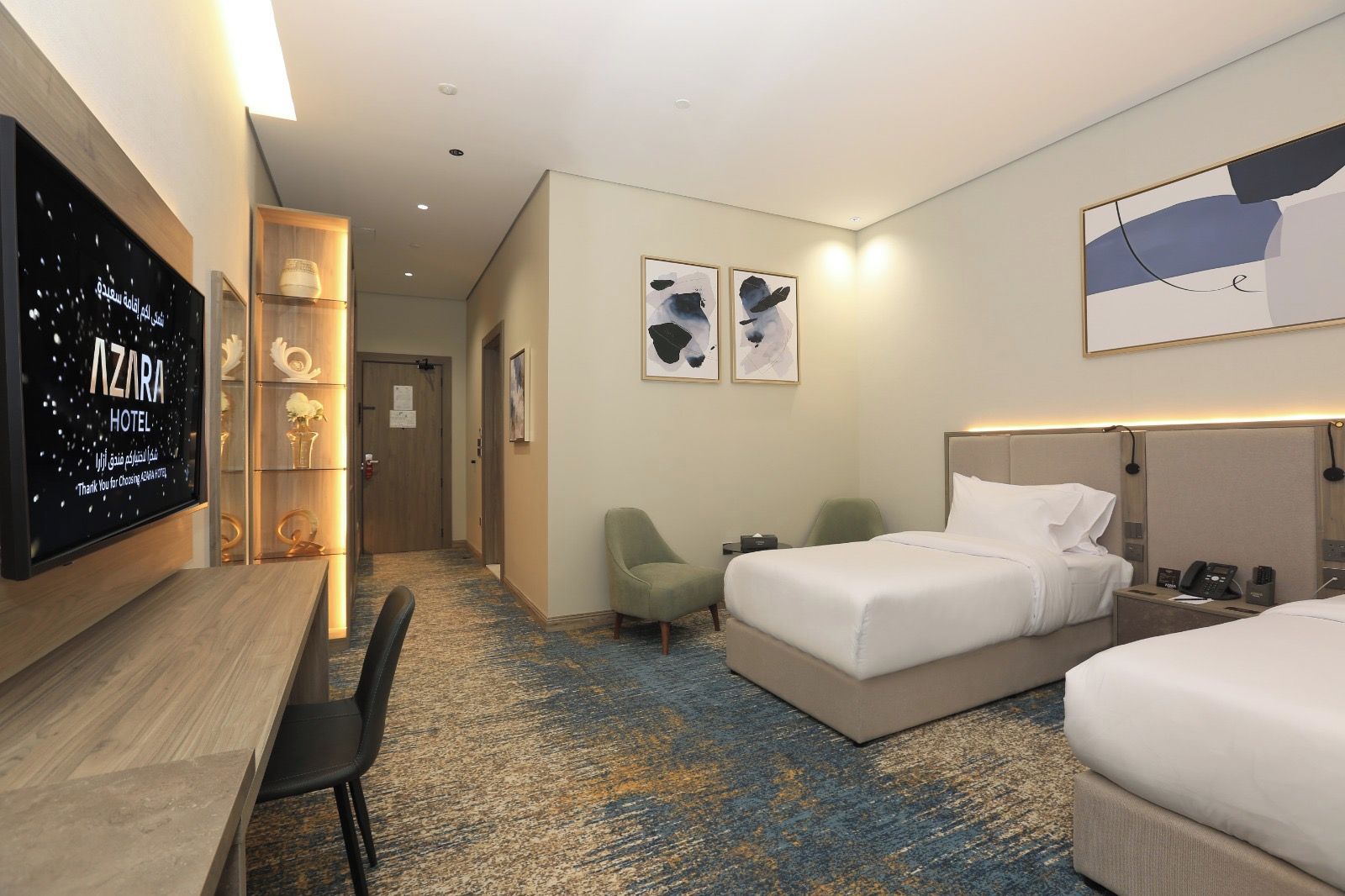 A hotel room with a bed, bedside tables, a desk, a chair, a television, and artwork on the walls.