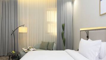 Een hotelkamer met een groot bed, een nachtkastje met een lamp en een raam met gordijnen.