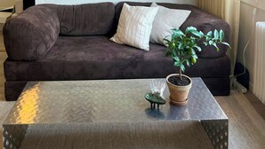 Una sala de estar con un sofá marrón oscuro, una mesa de centro de vidrio y una planta en maceta.