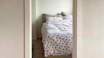 Un estrecho pasillo conduce a un dormitorio con una cama, una lámpara colgante y suelo de madera.