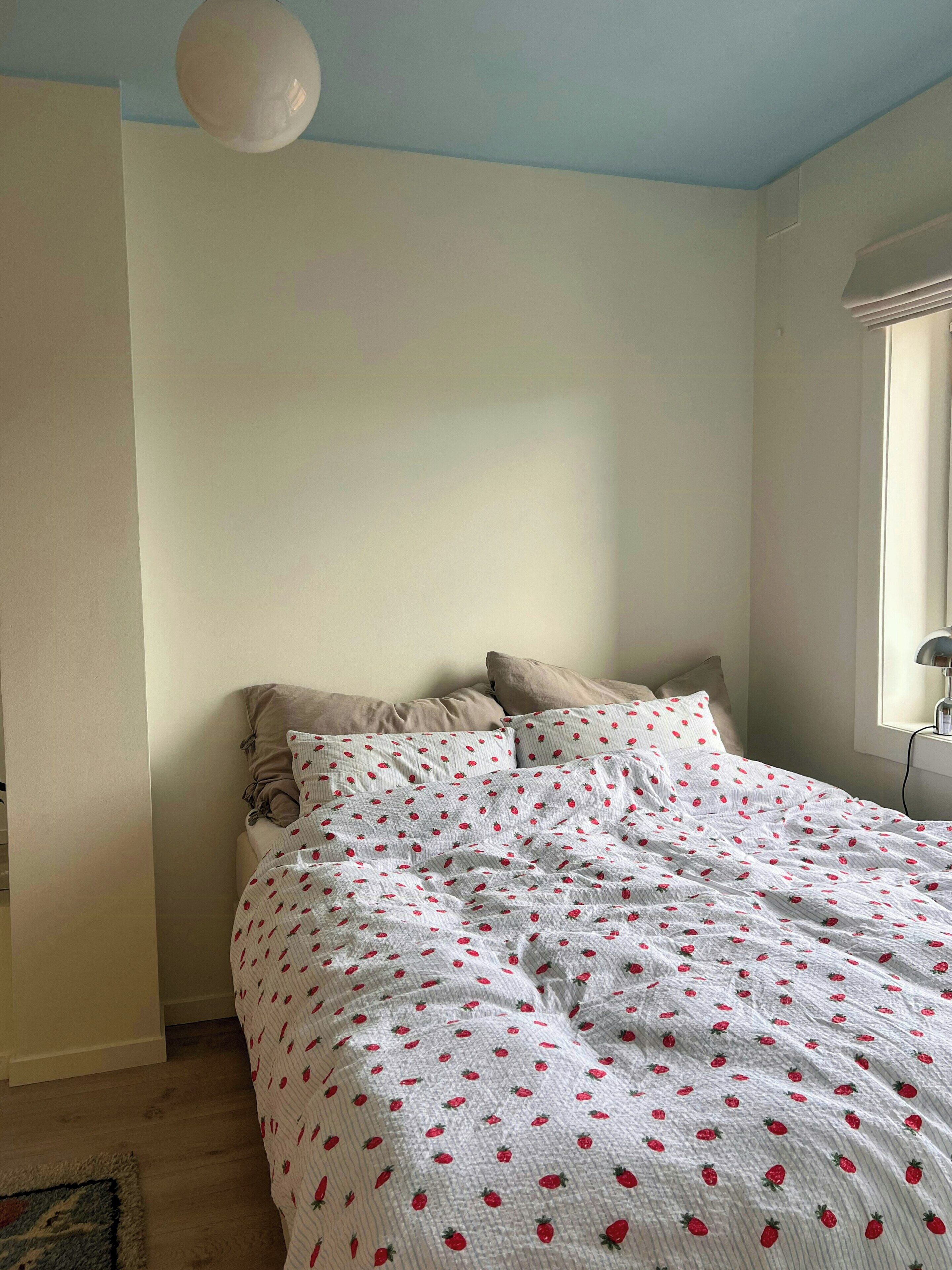 Une chambre à coucher avec un lit, des oreillers, une fenêtre et une lampe.