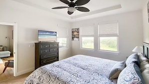 Un dormitorio con cama, cómoda, televisor y ventanas.