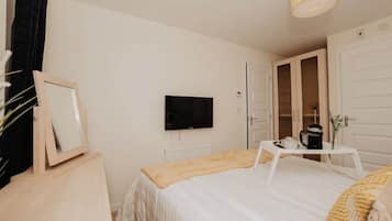 A bedroom with a bed, a television, a white door, and a small table with a cup and a plant.