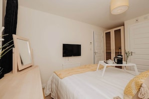 A bedroom with a bed, a television, a white door, and a small table with a cup and a plant.