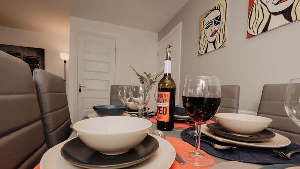 A dining table set with plates, bowls, cutlery, and a bottle of wine. - Coyle House sleeps 7 free parking (Northamptonshire)