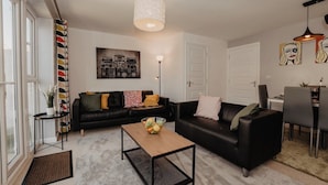 A modern living room with a black leather sofa, a coffee table, and a dining area with a table and chairs. - Coyle House sleeps 7 free parking (Northamptonshire)