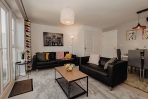 Uma sala de estar moderna com um sofá de couro preto, uma mesa de centro e um espaço de jantar com mesa e cadeiras.
