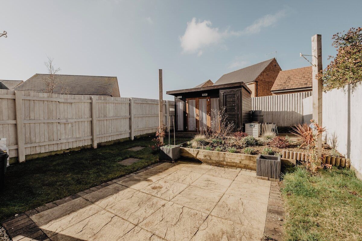 A backyard with a paved patio, a wooden fence, and a garden with various plants.