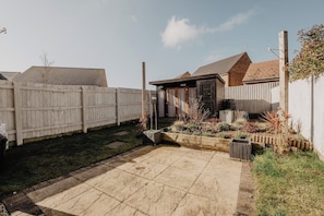 A backyard with a paved patio, a wooden fence, and a garden with various plants.