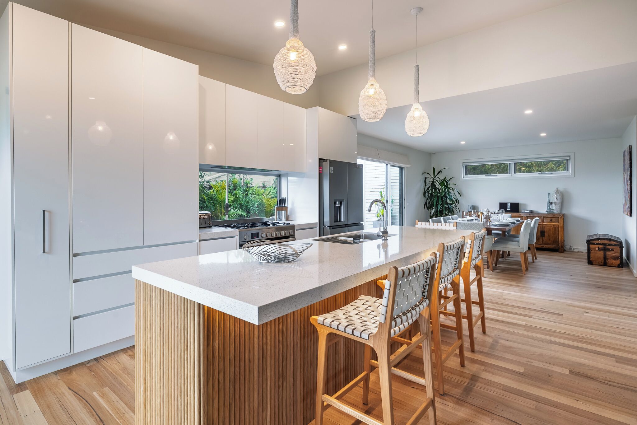 A modern kitchen with a central island, wooden bar stools, and pendant lighting.