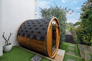 A wooden sauna with a sloped roof, a wooden door, and a small window. - Coastal Haven on Baker (Ocean Grove)