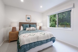 Un dormitorio con una cama grande, dos mesitas de noche, una ventana con vistas a zonas verdes y un cuadro en la pared.