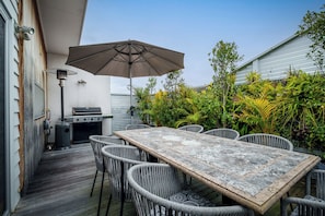Un patio exterior con mesa y sillas, una parrilla y un gran paraguas.