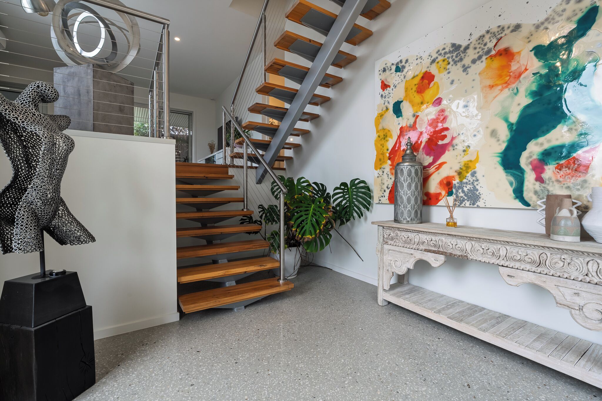 Un intérieur moderne agrémenté d’un escalier, d’une sculpture, d’un tableau abstrait aux couleurs vives et d’une console décorative.