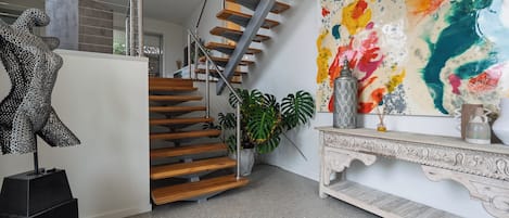 Un interior moderno con una escalera, una escultura, un cuadro abstracto colorido y una consola decorativa.
