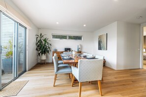 A modern dining area with a wooden table, chairs, and a large potted plant. - Coastal Haven on Baker (Ocean Grove)