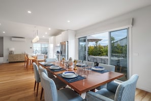 Un comedor moderno con una mesa de madera dispuesta para seis personas, rodeada de sillas, y vistas al exterior a través de amplios ventanales.