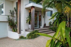 A modern house with a covered porch, a stone statue, and various plants. - Coastal Haven on Baker (Ocean Grove)