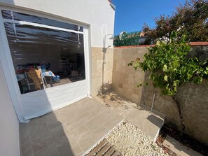 A residential property with a sliding glass door, a tiled patio, and a stone wall with greenery. - Villa for 9 people near La Gautrelle Beach, ideally located (Saint-Georges-d'Oléron)
