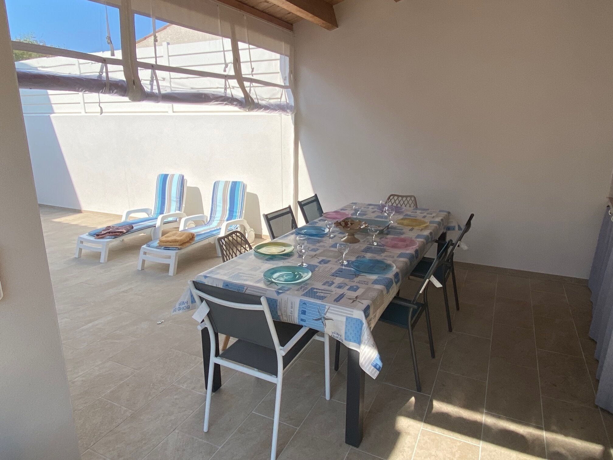 An outdoor dining area with a table set for six, surrounded by chairs, under a covered patio.