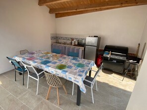 A dining area with a table set for four, a kitchen with a refrigerator and stove, and a barbecue grill. - Villa for 9 people near La Gautrelle Beach, ideally located (Saint-Georges-d'Oléron)