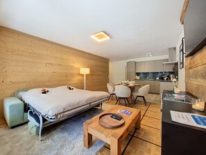 Une chambre d’hôtel compacte comprenant un lit, un bureau, une chaise, un petit coin cuisine et un mur en bois.
