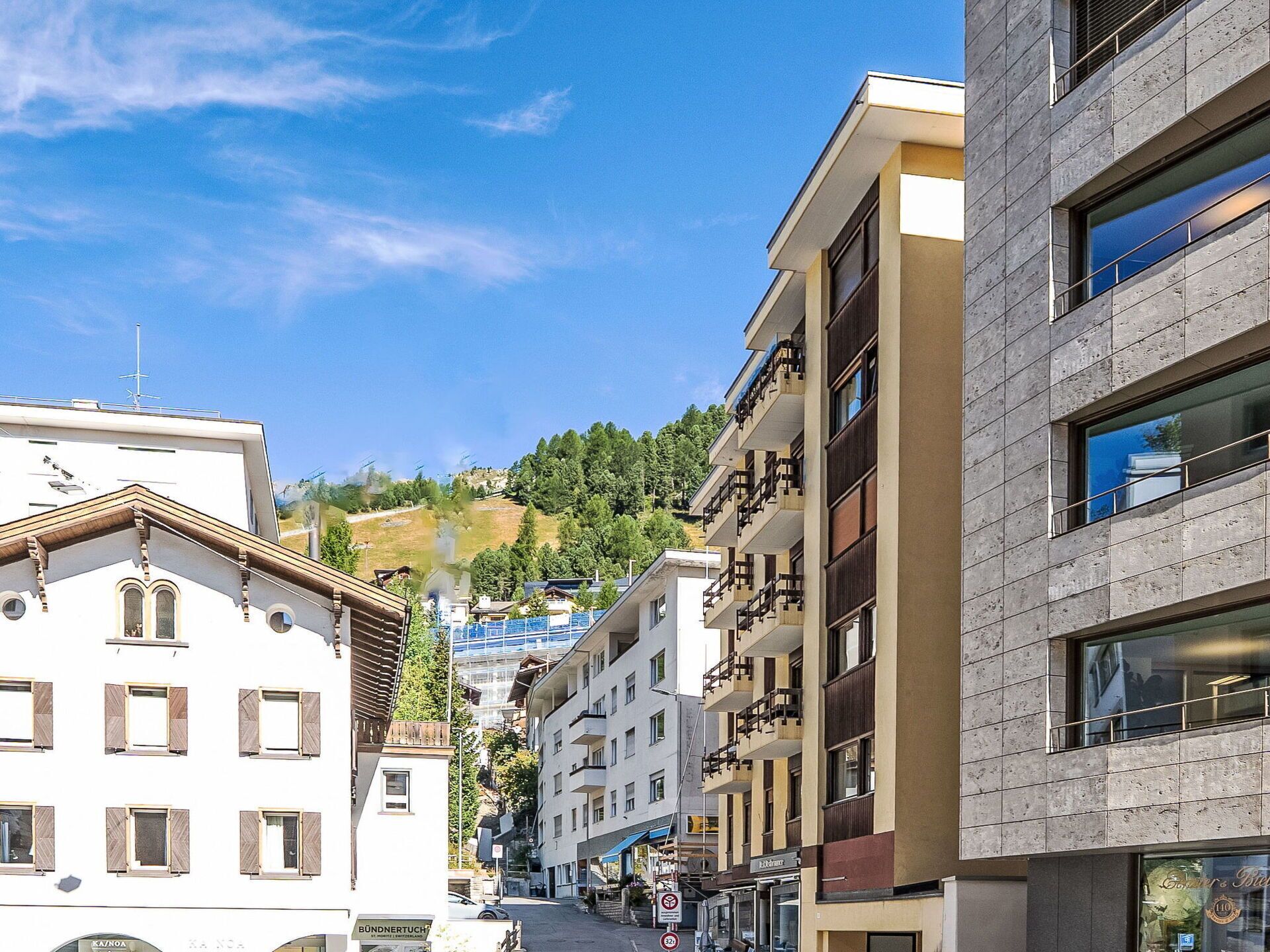 Une vue de rue avec des bâtiments, un ciel dégagé et un paysage vallonné en arrière-plan.