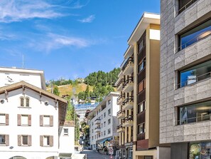 Vista de una calle con edificios, cielo despejado y un paisaje montañoso al fondo.