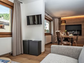 Una sala de estar moderna con un televisor de pantalla plana montado en la pared, un comedor con mesa y sillas, y un ventanal con cortinas.