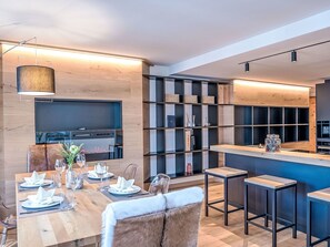 A modern dining area with a wooden table set for four, a bar area with stools, and a kitchen with a built-in oven and microwave. - Beautiful apartment for 4 guests with WIFI, TV, balcony, pets allowed and panoramic view (Saint Moritz)