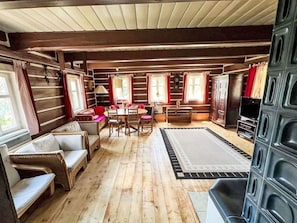 Interior de uma cabana de toras com área de jantar, assentos e uma televisão.