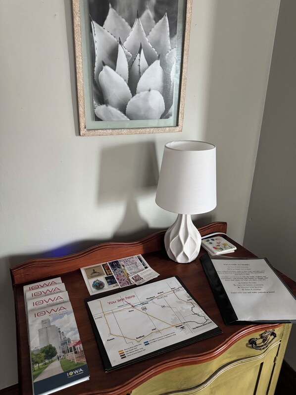 A room with a wooden desk, a map, a framed picture, and a white lamp.
