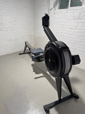 A stationary exercise bike with a digital display, positioned against a white brick wall in a room with a concrete floor.