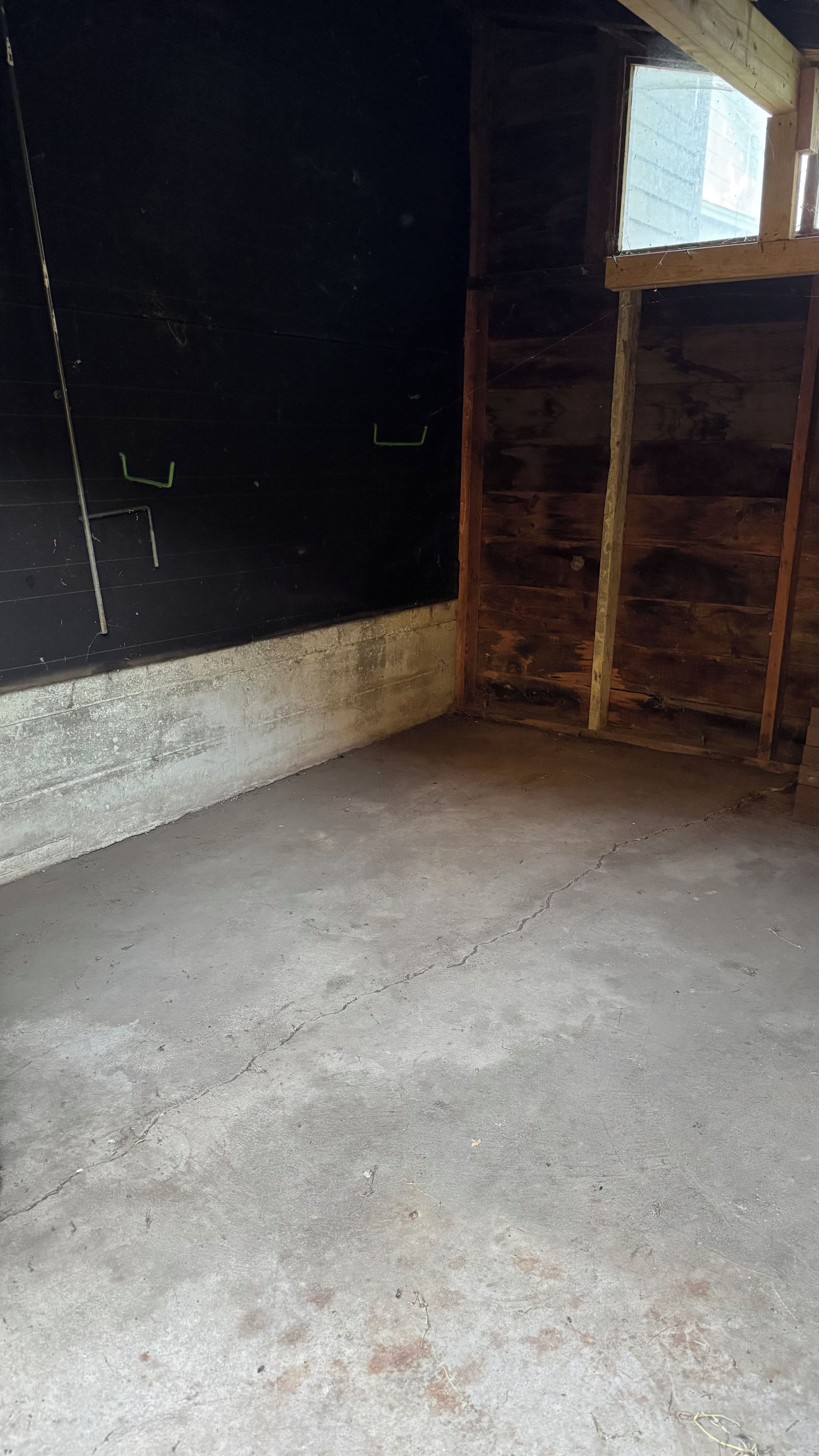 A room with a concrete floor, wooden walls, and a window.