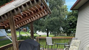 Une terrasse en bois avec mobilier d’extérieur, notamment des chaises et un espace barbecue abrité.